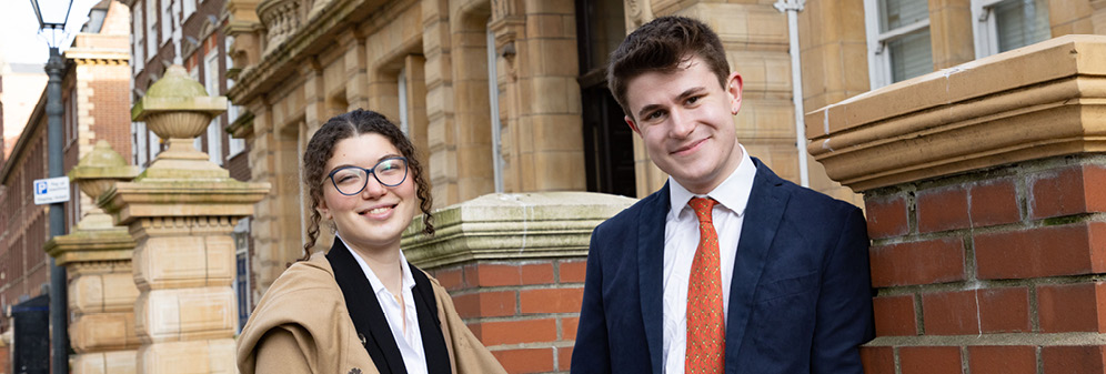 Female and male student smiling, wearing smart clothes, stood outside an old building in Bristol